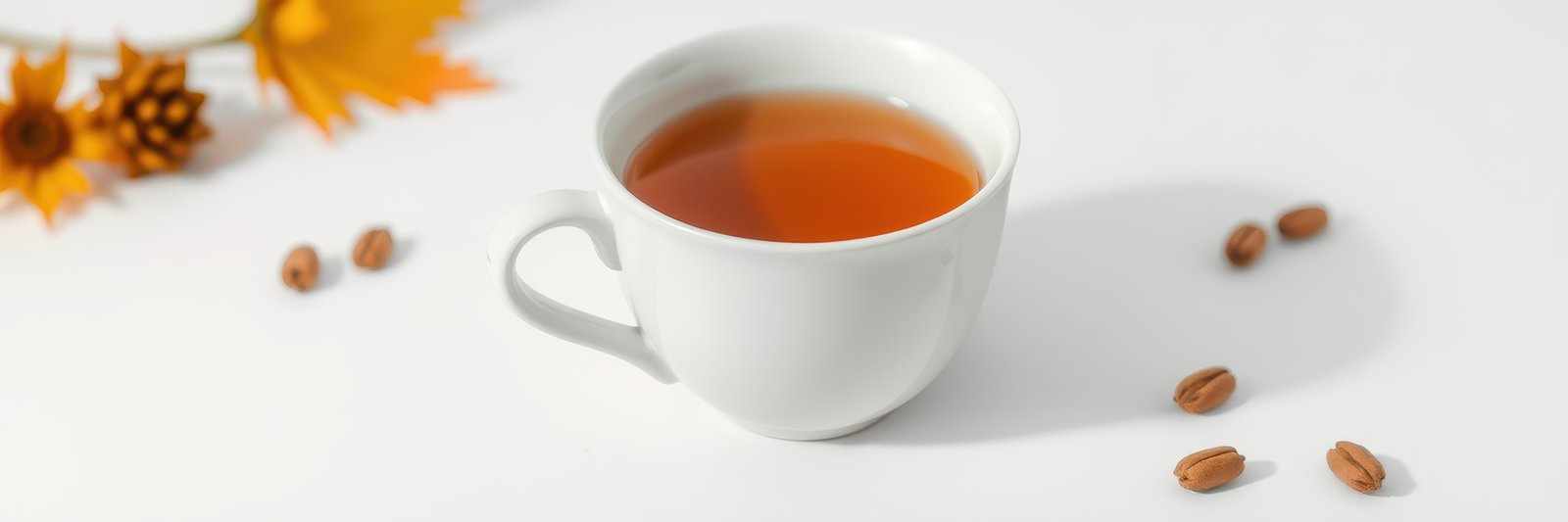 Warm tea in a white cup with autumn leaves and nuts on a bright white table
